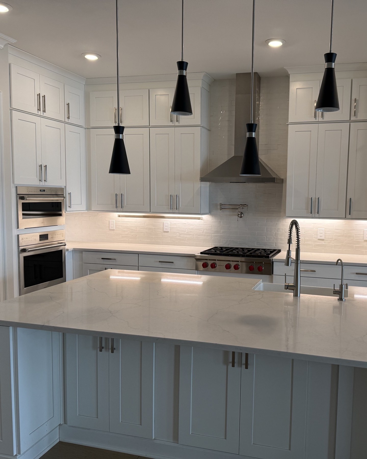 Finished kitchen remodel in Alpharetta, GA: white shaker cabinets, a large quartz island with prep sink, a stainless Wolf range under a chimney hood, and a light ceramic backsplash